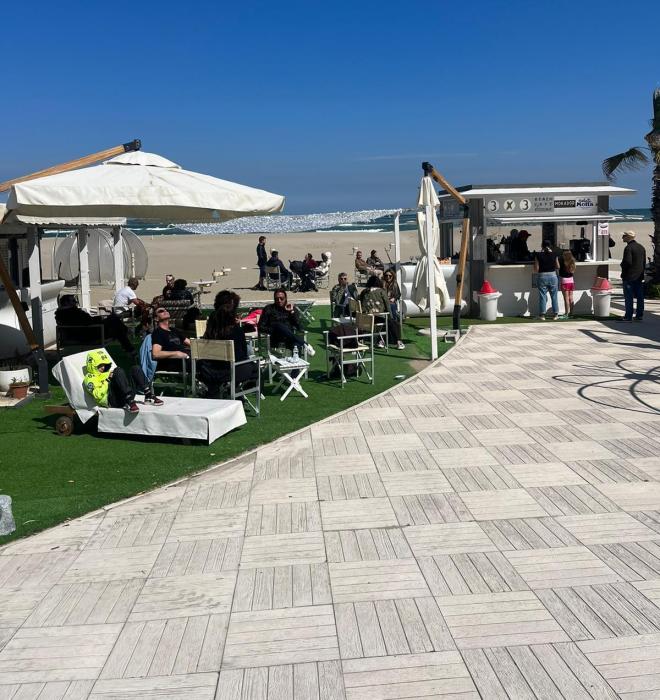Persone rilassate in spiaggia sotto ombrelloni, cielo limpido.