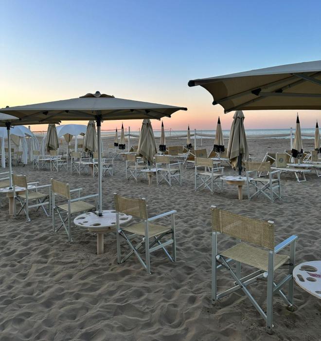Spiaggia al tramonto con sedie e ombrelloni, atmosfera serena e rilassante.