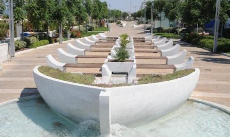 Fontana moderna con piante e acqua in un viale alberato.