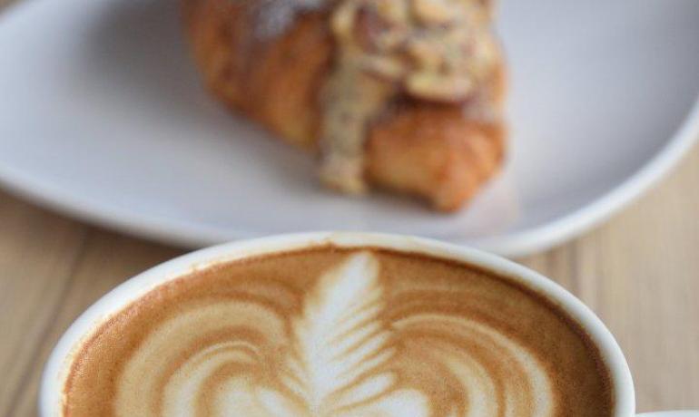 Cappuccino con latte art e croissant su piatto bianco.