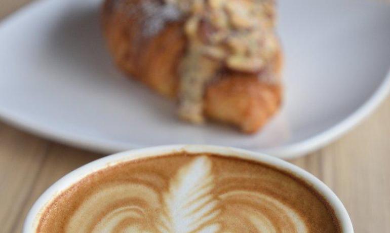 Cappuccino con latte art e croissant su piatto.
