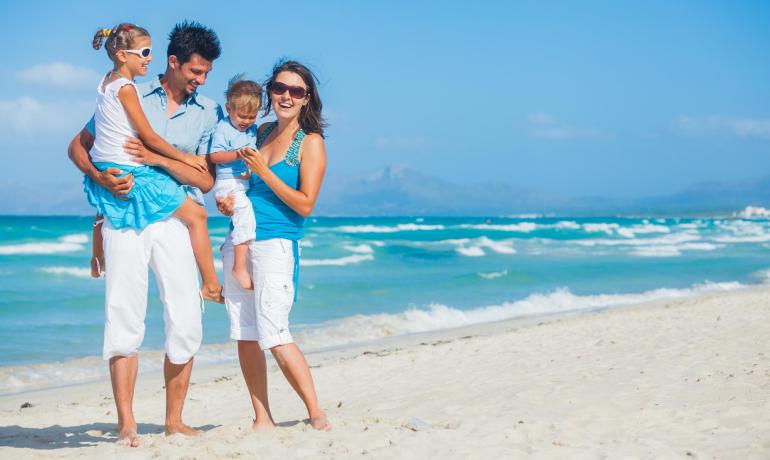 Famiglia felice sulla spiaggia con mare azzurro e cielo sereno.