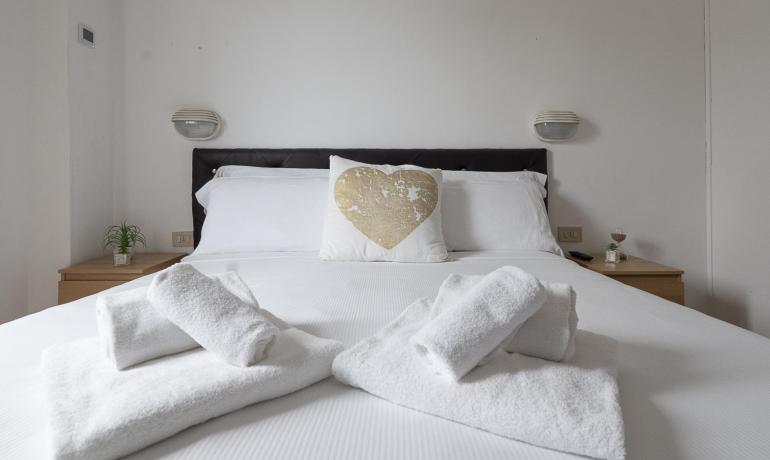 Letto accogliente con cuscino a cuore, asciugamani morbidi e atmosfera rilassante.