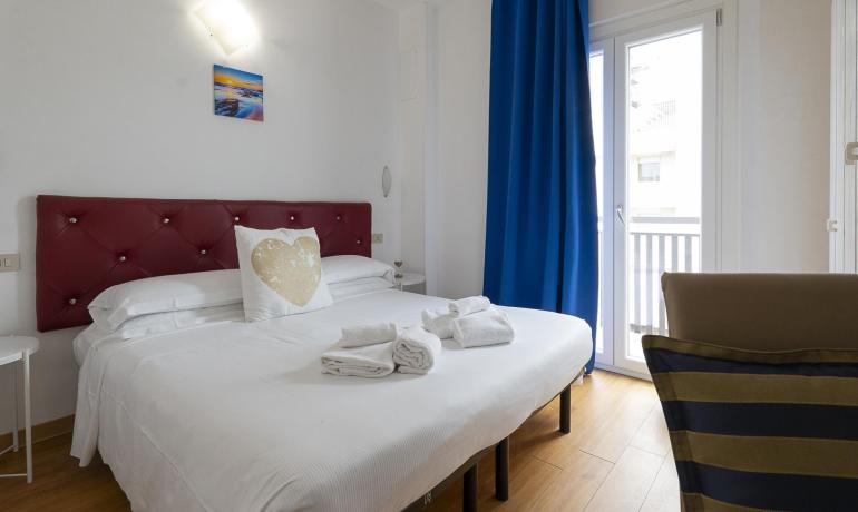 Camera accogliente con letto bianco, cuscino decorativo e tende blu.