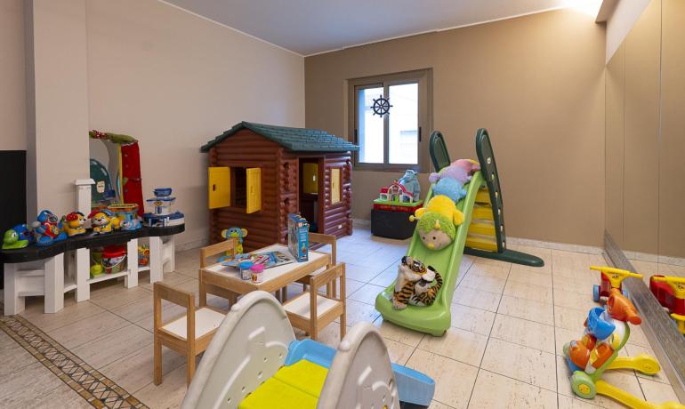Sala giochi con scivolo, casetta e giocattoli colorati.
