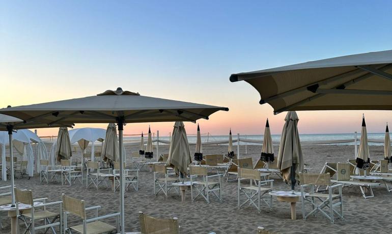 Spiaggia al tramonto con sedie e ombrelloni, atmosfera serena e rilassante.