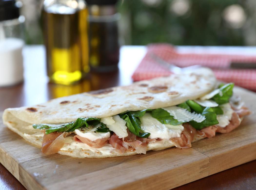 Piadina fragrante con prosciutto, formaggio e rucola su tagliere di legno.