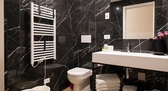Bagno elegante con pareti in marmo nero e lavabo moderno, decorato con fiori.